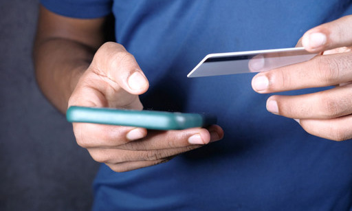 A man holding a smartphone in one hand and a credit card in the other.