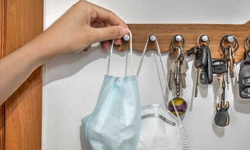 Someone hanging a mask on a key rack, next to another mask and four sets of keys.