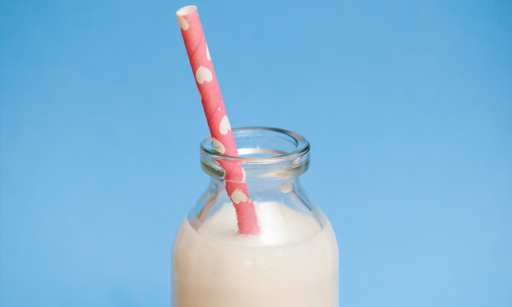A milk bottle with a pink straw in it.