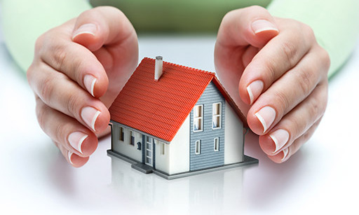 A model house on a table with someone’s hands either side, protecting it.