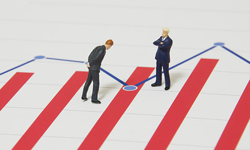 Two tiny model men in business suits on top of a printed graph.