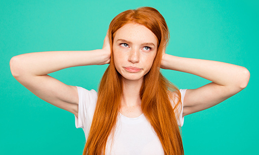 A red haired woman holding her ears and rolling her eyes.